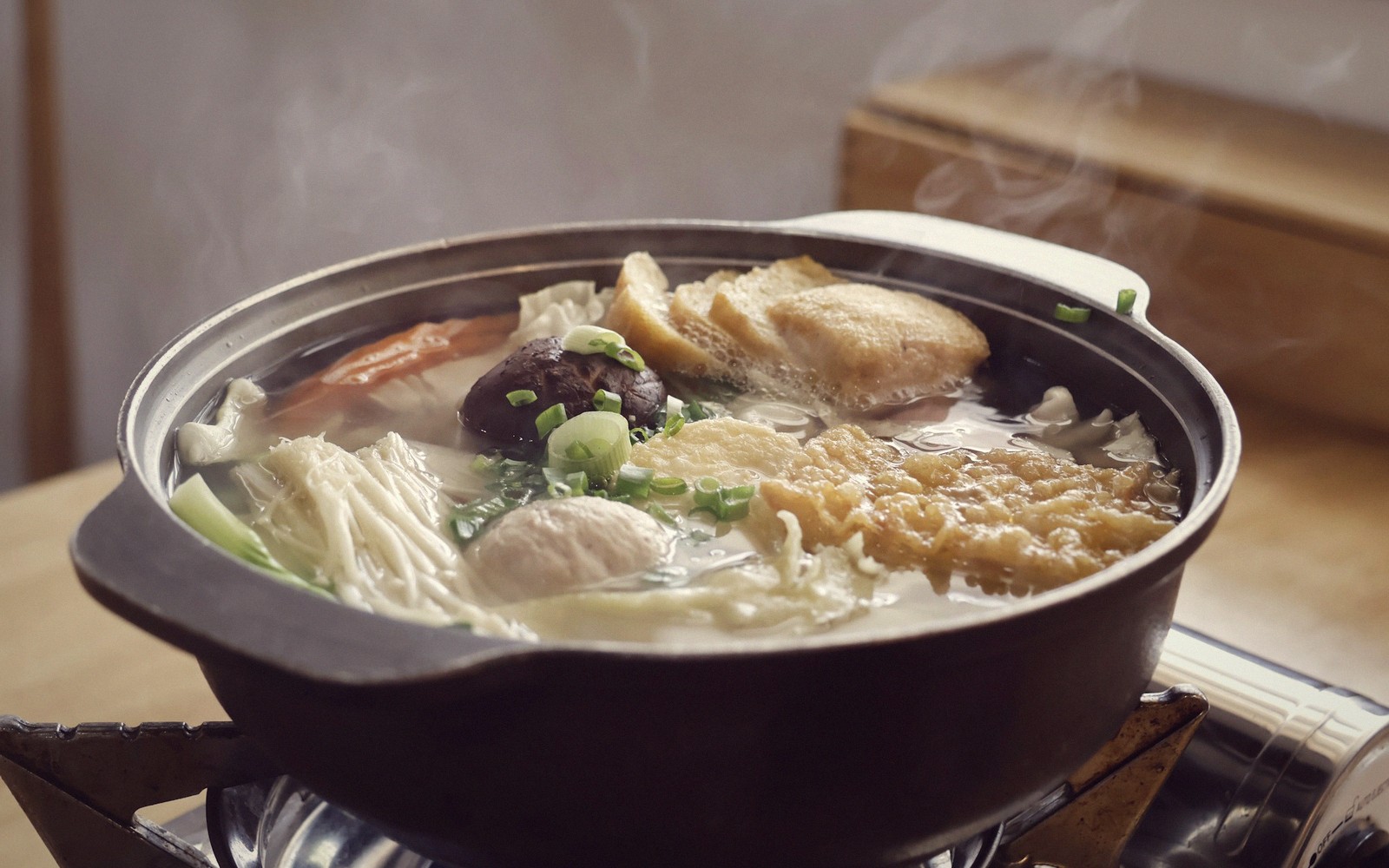 Steaming hotpot with mushrooms, tofu skin, fish balls and scallions in a clay pot