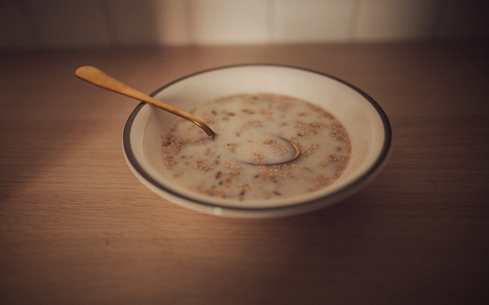 A gold spoon rests in a bowl of milky grain porridge on a wooden table