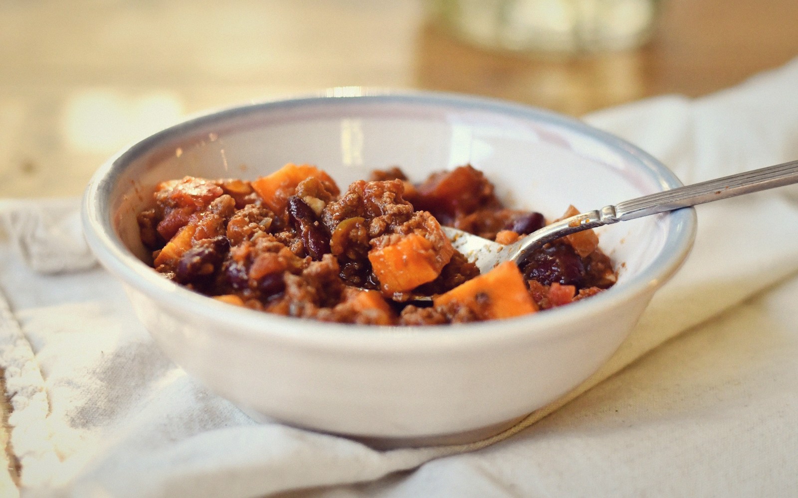 Bowl of chili with beans, ground meat and sweet potato chunks, spoon resting inside