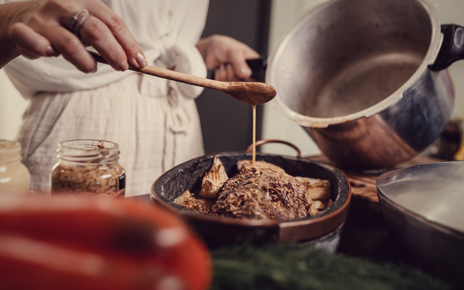Spooning sauce over a roasted dish with a wooden spoon in a kitchen