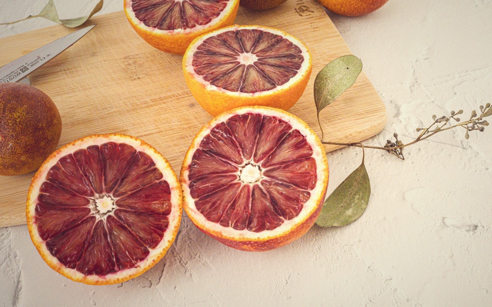Halved blood oranges reveal deep red flesh on a wooden cutting board
