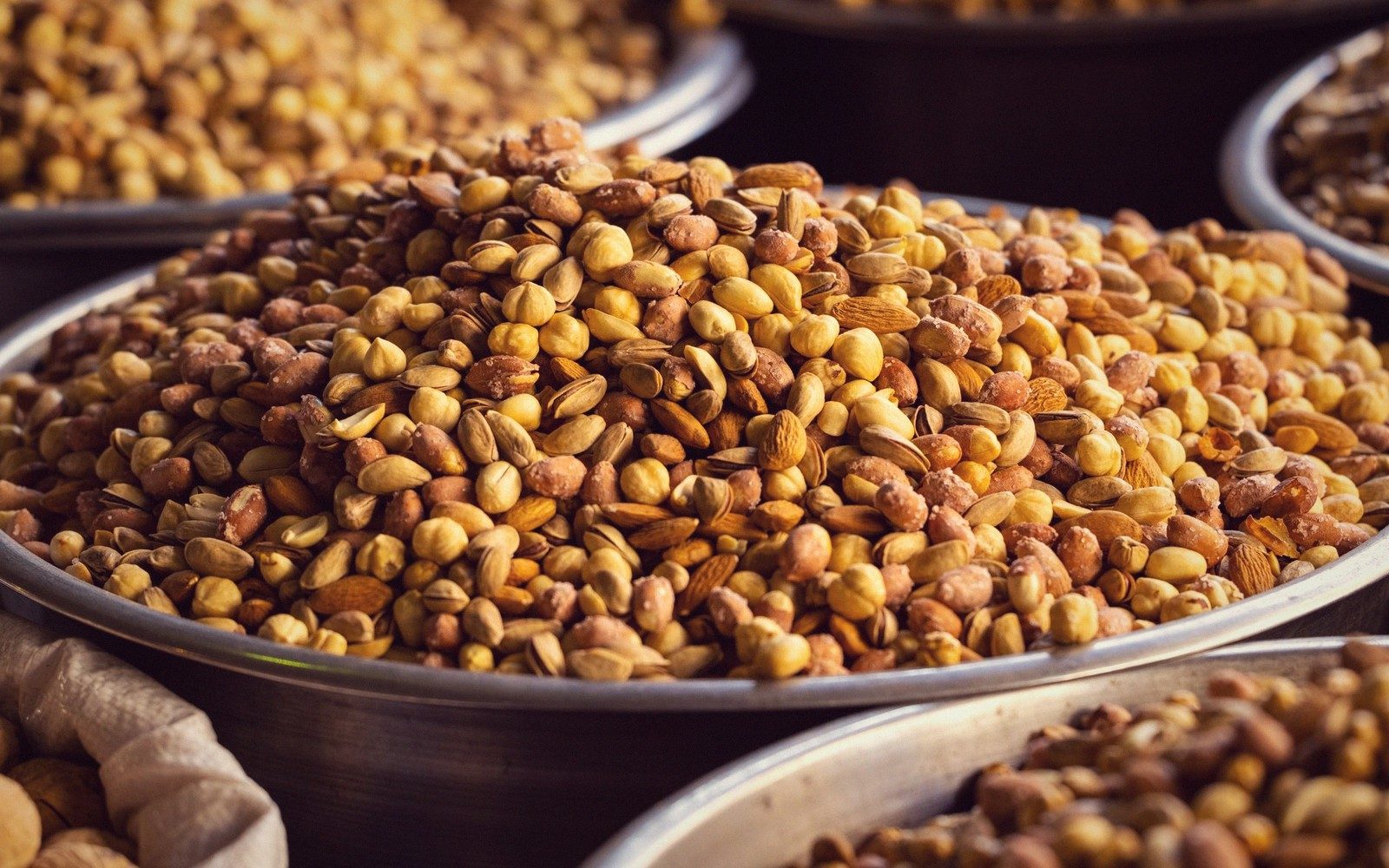 Metal bowls piled with roasted peanuts, pistachios and almonds at a market stall